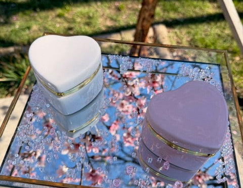Two heart shaped containers, one white and one purple, held against a floral background.