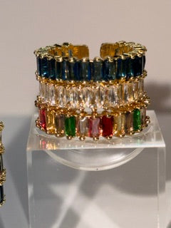 A gold-tone adjustable rings with multiple rows of rectangular gemstones in blue, clear, yellow, green, and red, displayed on a clear acrylic stand.